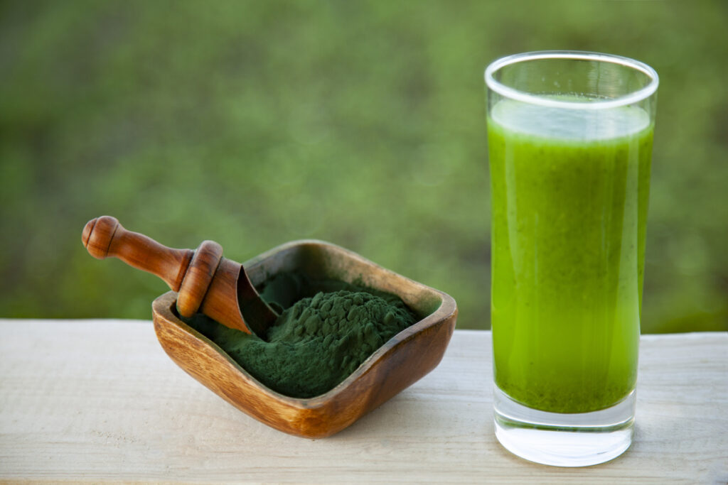 Green smoothie with spirulina on green grass background