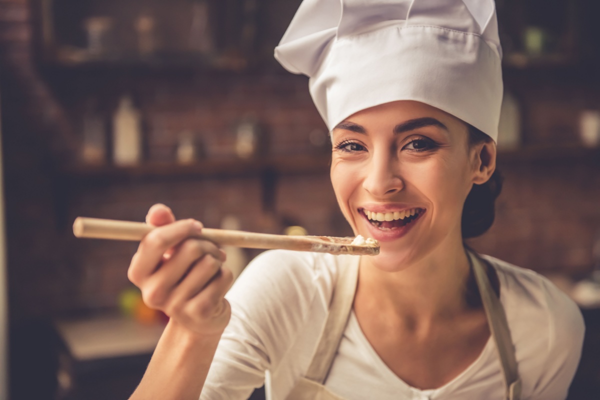 woman chef happy tasting food off wooden spoon