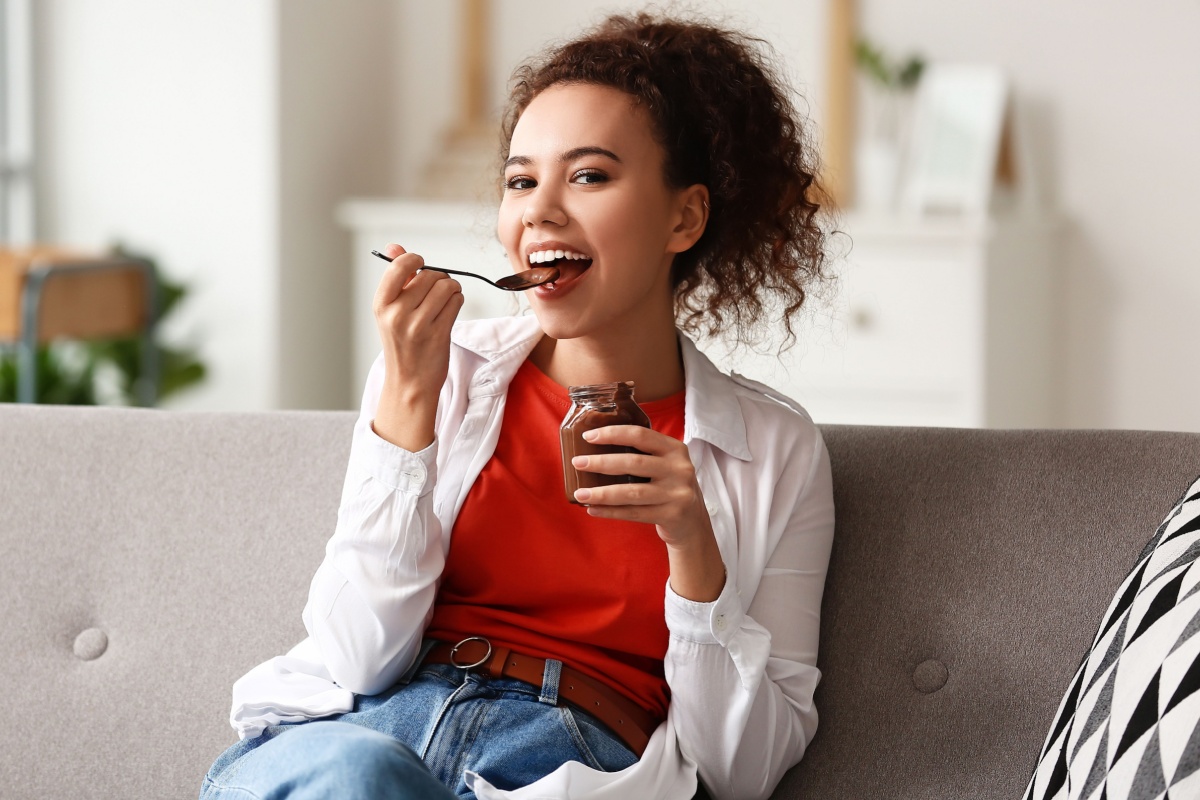 woman eating chocolate paste out of jar on couch