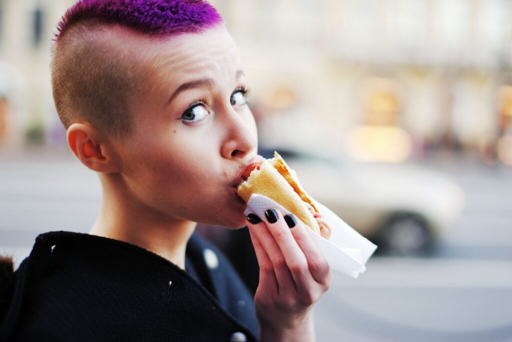 woman with purple hair eating hot dog