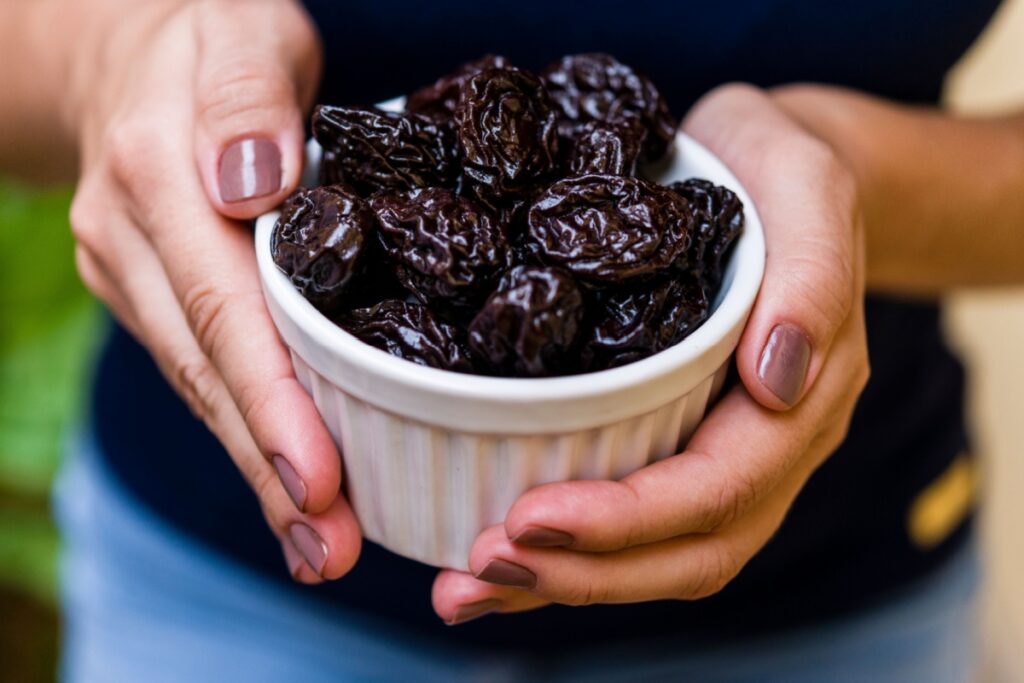 woman's hands holding bowl of prunes fruit