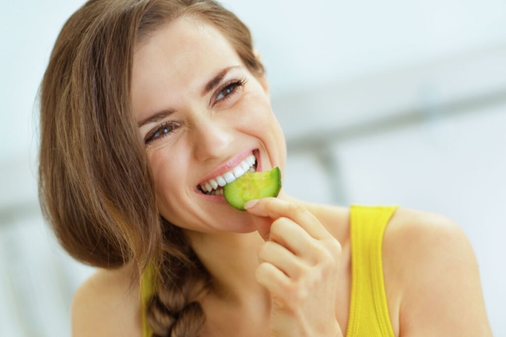 young woman eating cucumber in kitchen