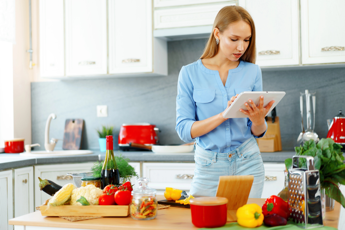 Young beautiful caucasian woman cooking and using her digital tablet in kitchen at home