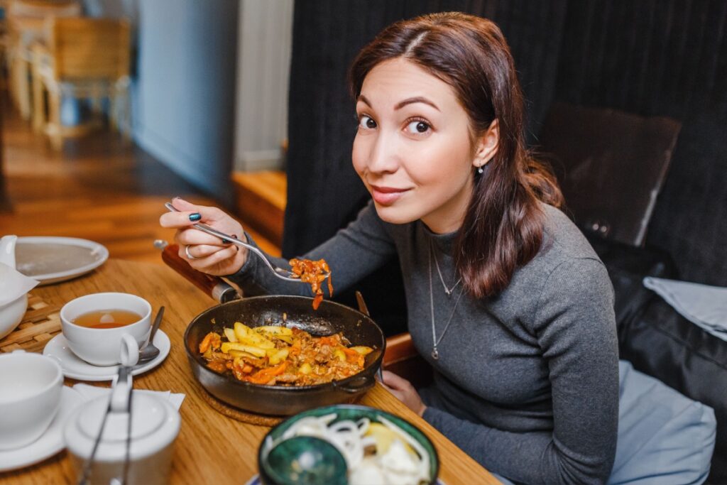 Asian woman eating meat from a frying pan in restaurant dinner