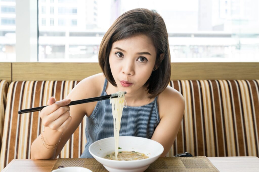 Asian woman eating noodles chopsticks in restaurant