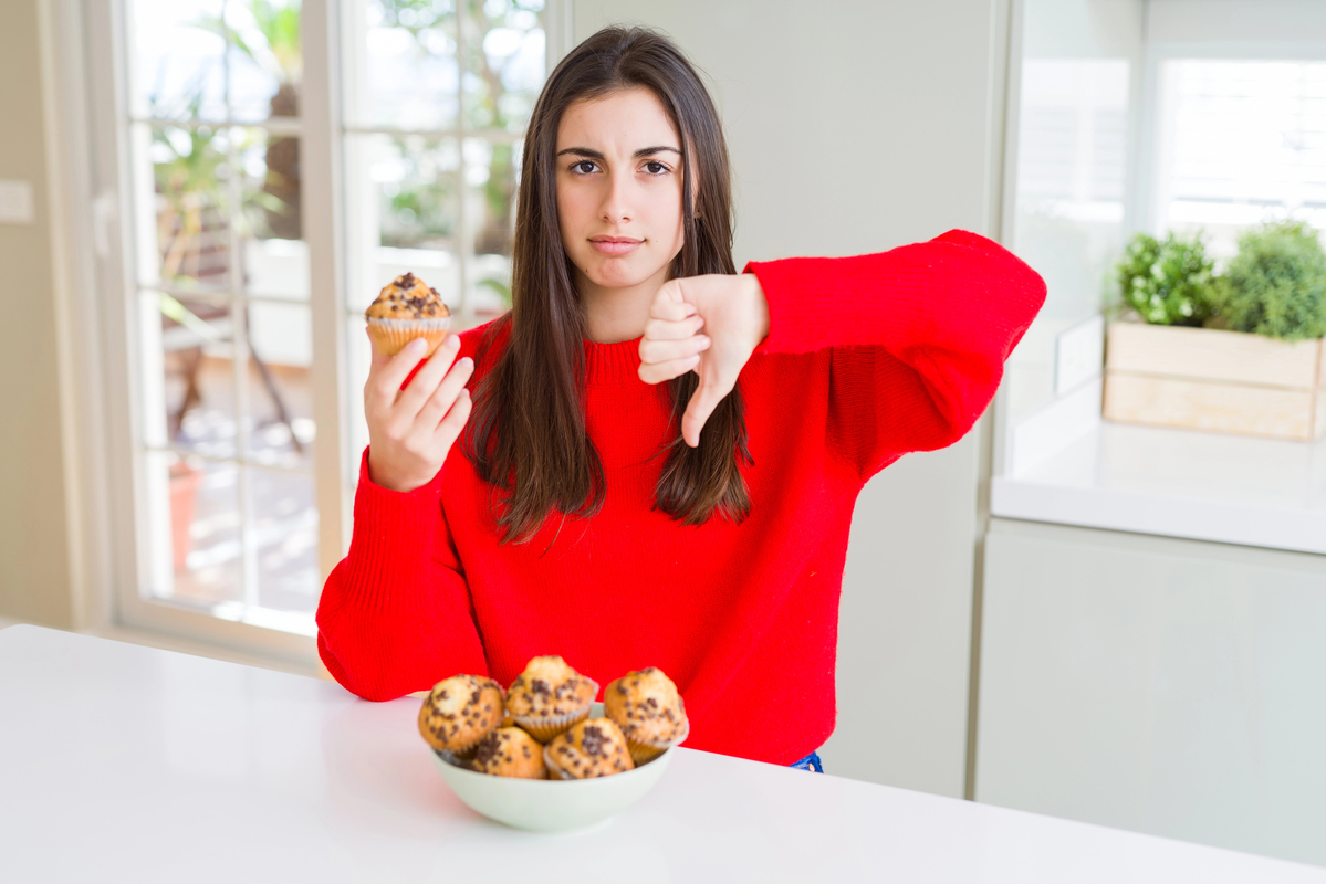 Beautiful young woman eating chocolate chips muffins with angry face