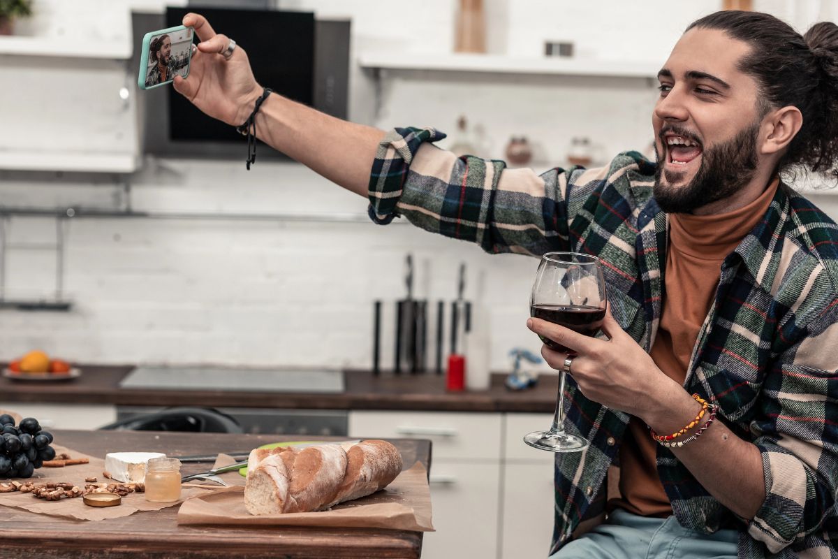 Happy man taking a selfie with a glass of wine while eating