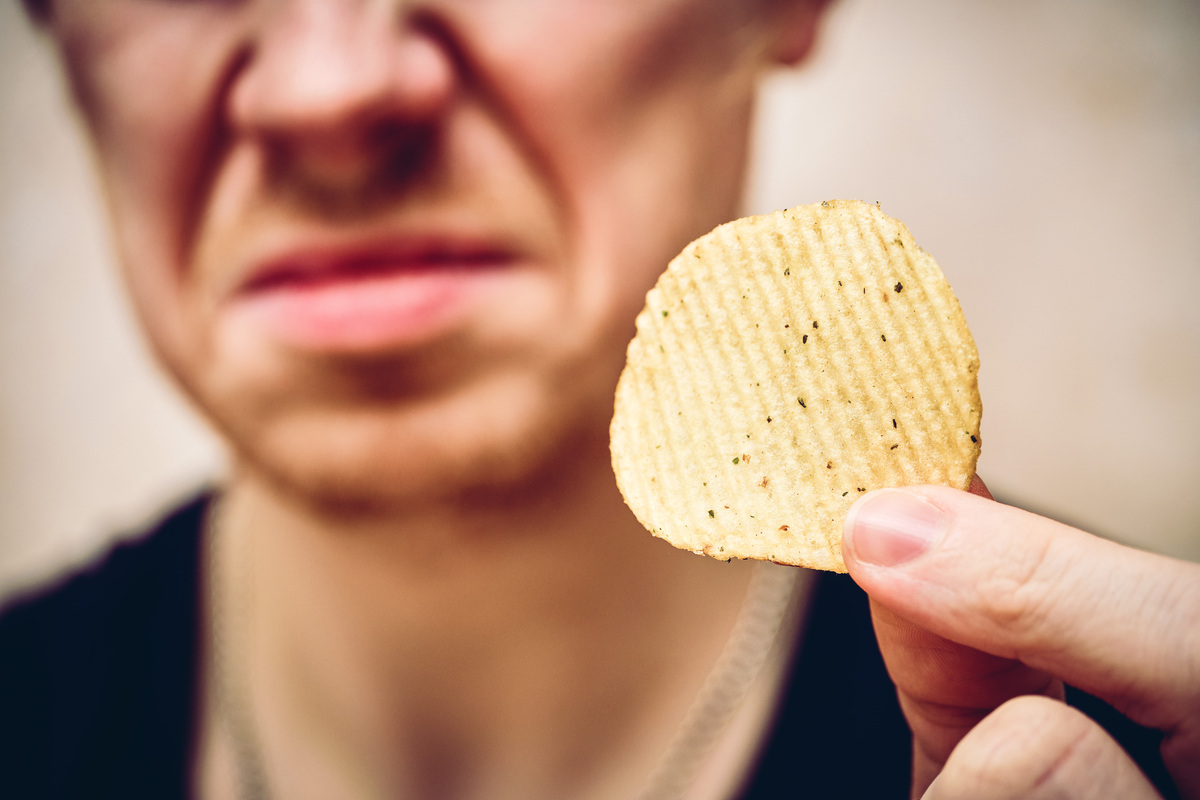 A man sits holding chips in his hand and he is disgusted by this. Close up.