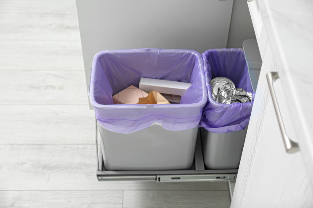 Open cabinet with full trash bins for separate waste collection in kitchen