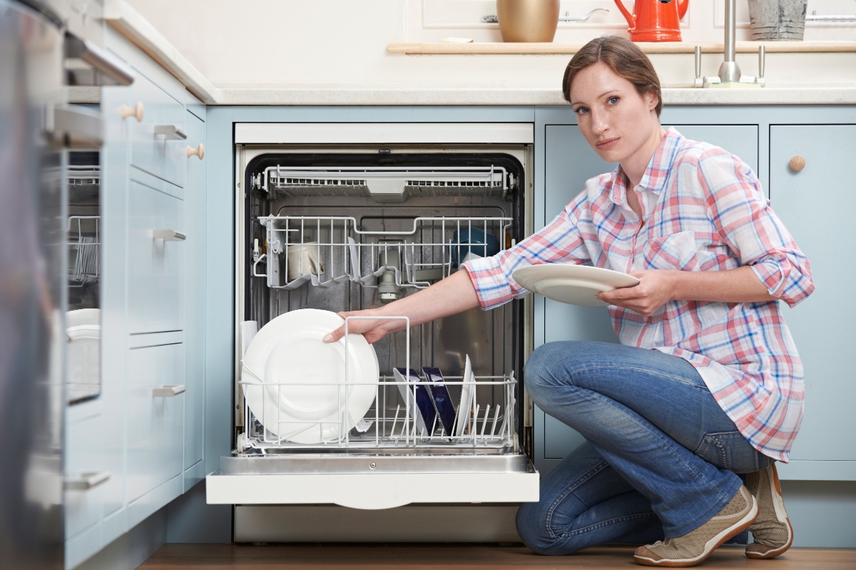 Woman Loading Dishwasher In Kitchen