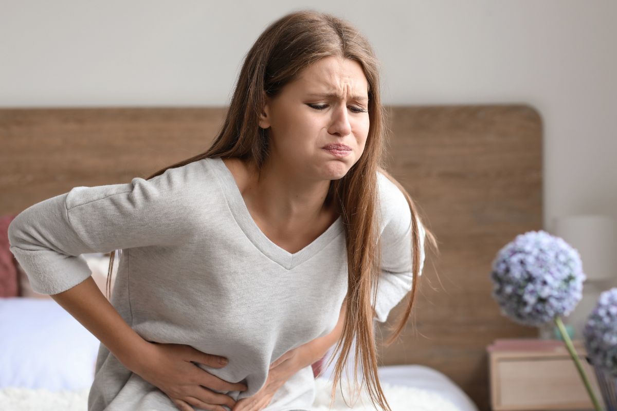 Woman holding her stomach upset sitting on a bed