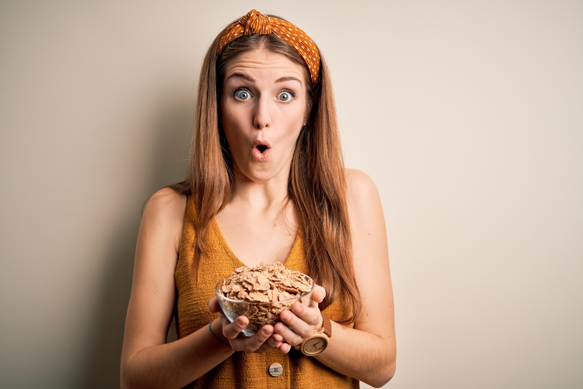 Young beautiful redhead woman holding bowl of healthy cornflakes