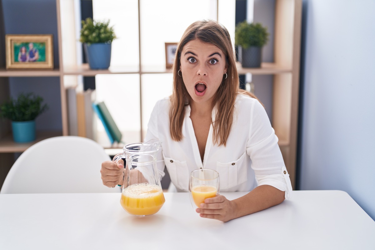 Young hispanic woman drinking glass of orange juice