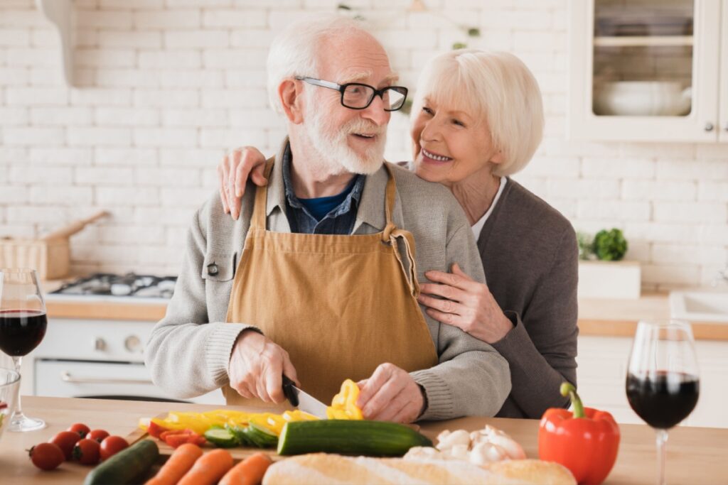 senior couple cooking in kitchen cutting vegetables