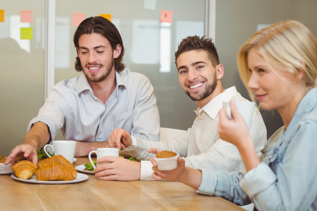 Portrait of businessman with colleagues having snacks in canteen at creative office