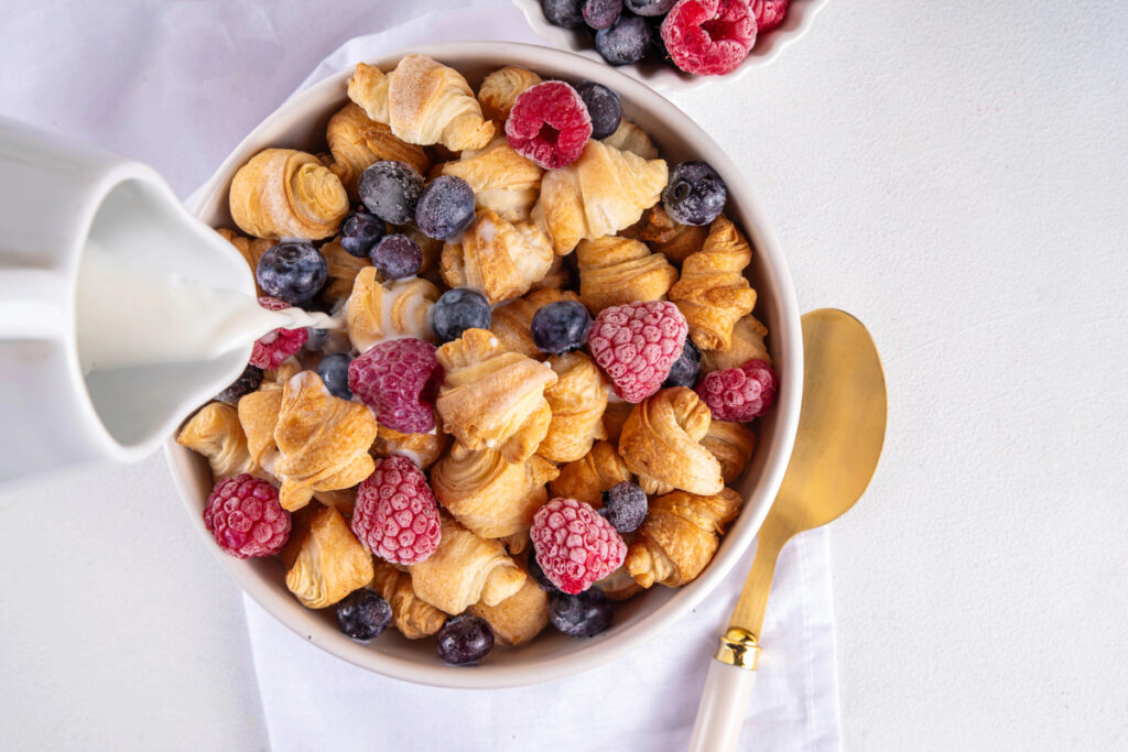 Tiny breakfast croissants cereals with fresh berries and milk. Bowl portions with trendy fresh baked mini petite croissants with raspberry and blueberry, dessert morning snack