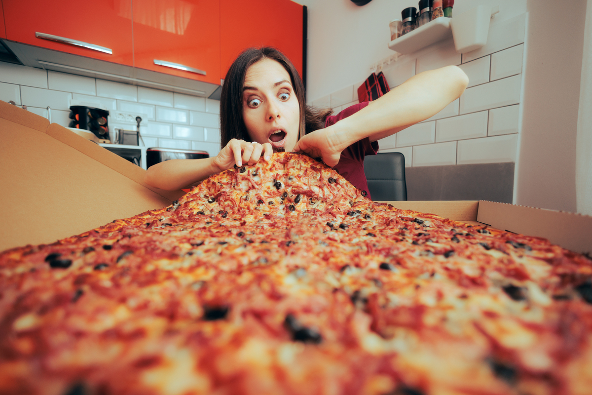 Hungry Woman Eating a Large Pizza by Herself in the Kitchen