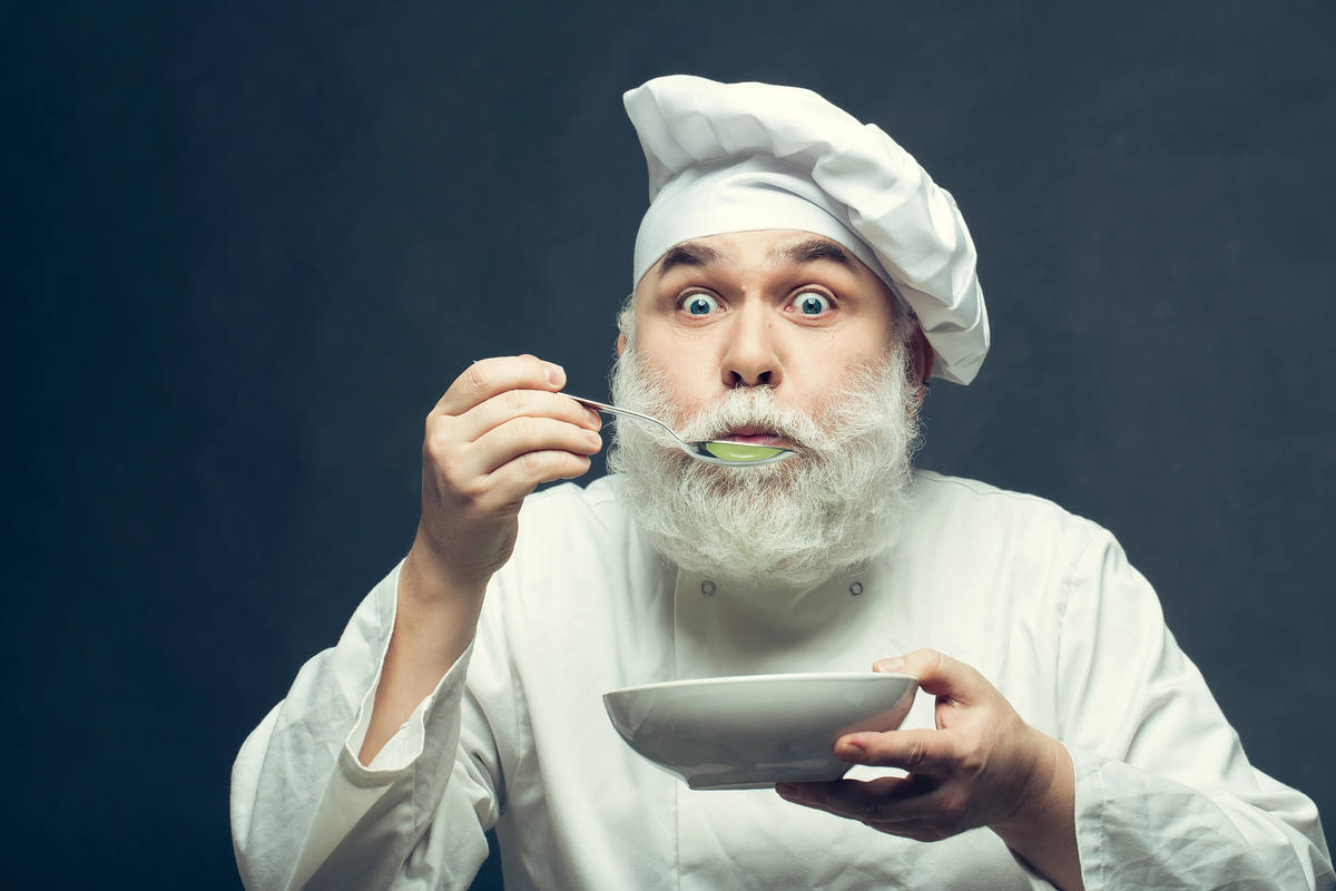 Man Bearded man cook in hat tasting food with spoon in studio on grey background tastes food