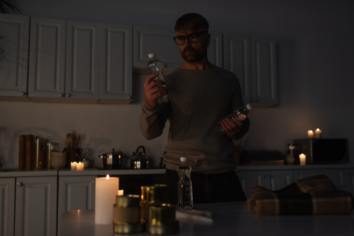 Man in eyeglasses holding bottled water near table with canned food