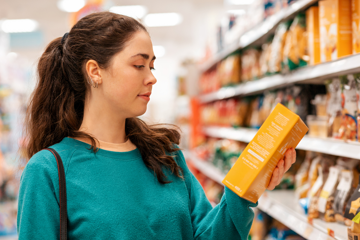 Portrait of a young Caucasian beautiful woman who reads the ingredients on the product packaging. Shelves with goods in a blur in the background. The concept of buying goods and shopping.