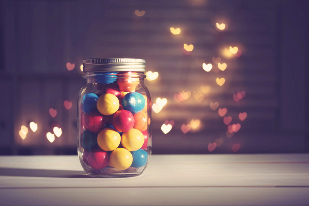 Colorful candies in a jar on heart shaped abstract light background