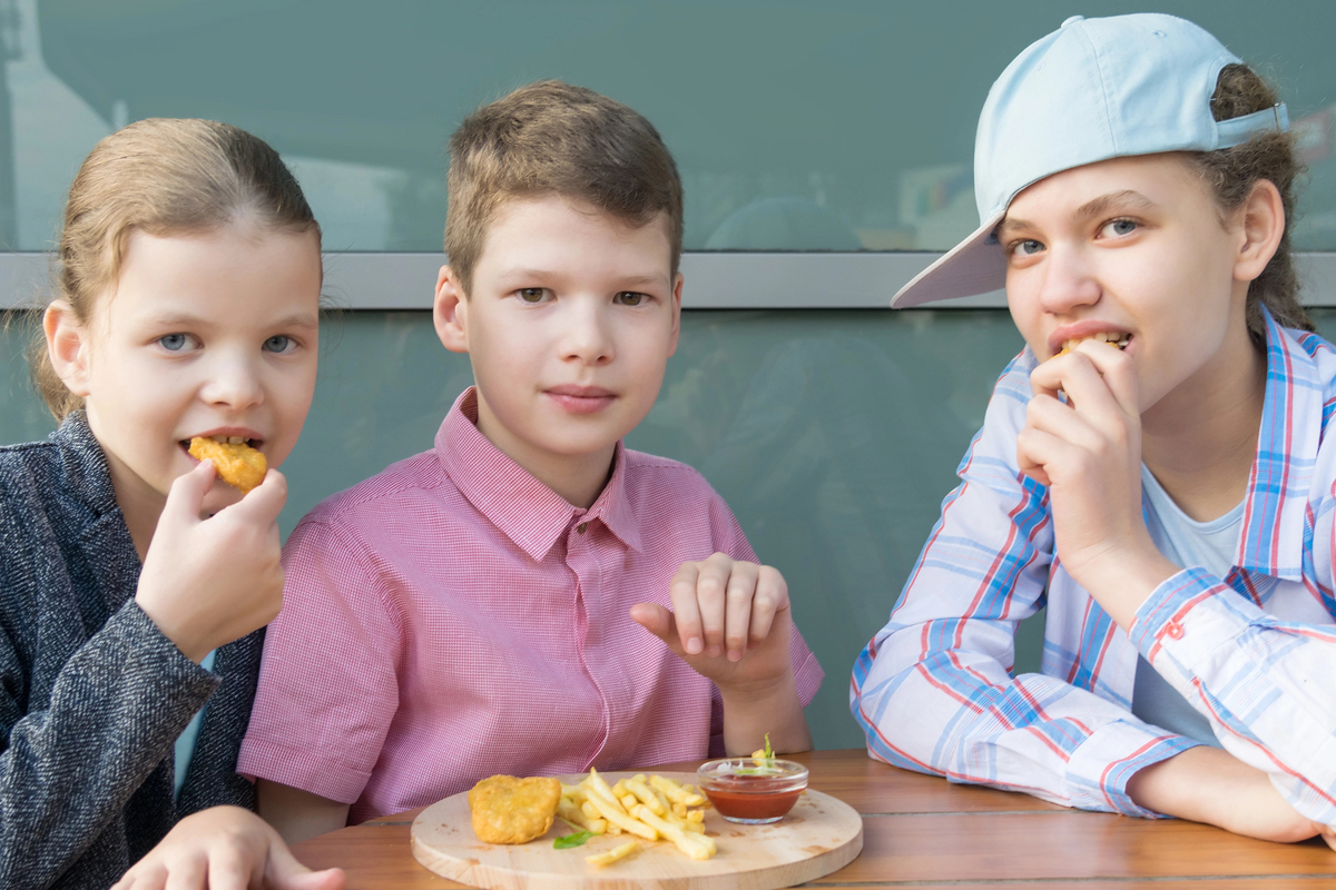 Schoolchildren boy and two girls in a cafe eat fast food sitting at a table