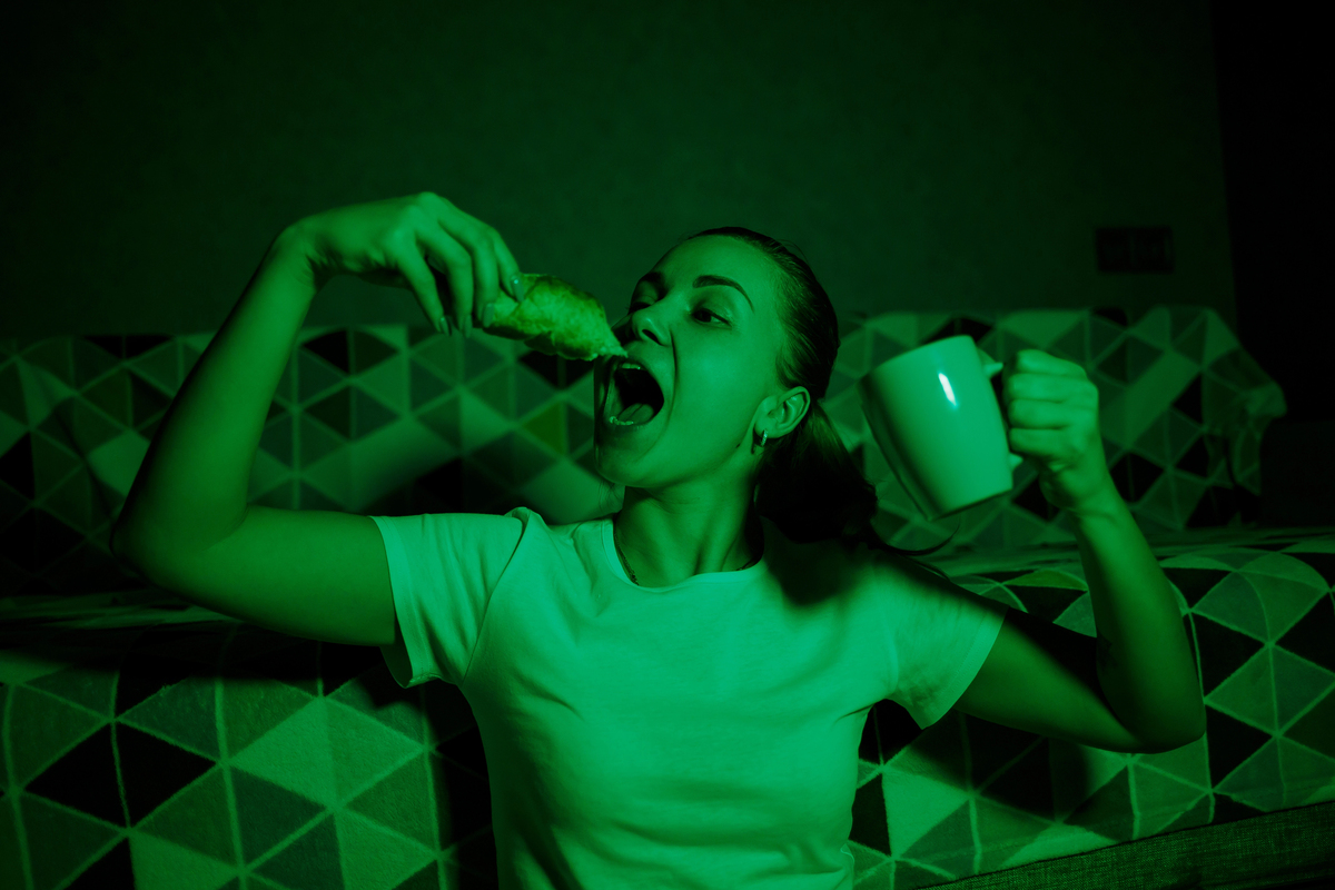 Young beautiful girl watching TV, eating a croissant and drinking tea.